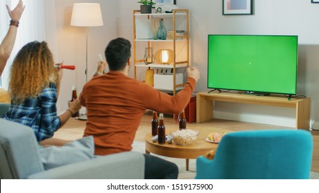 Three Sports Fans Sitting On A Couch In The Living Room Watch Green Chroma Key Screen TV Important Match, Using Horns, Cheering For Their Team And Celebrates Win Doing YES Gesture.