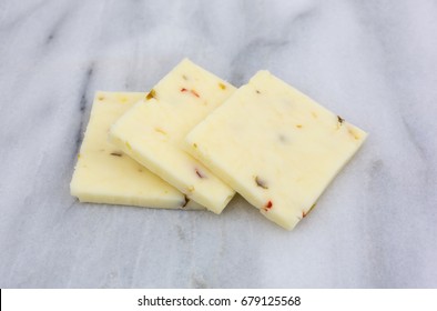 Three Square Slices Of Fresh Pepper Jack Cheese On A Gray Marble Cutting Board.