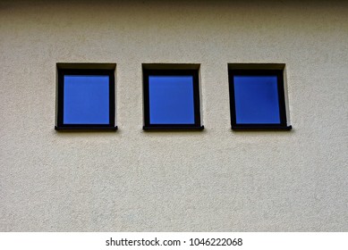 Three square small windows on the gray wall of the building