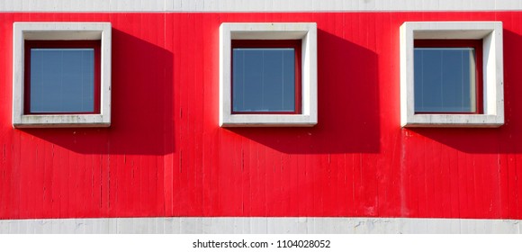 three square windows in the building with red wall