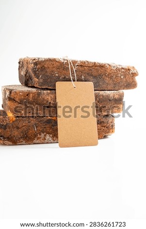Three stacked reclaimed rustic bricks on a white background with a blank kraft paper price tag hanging from them. Mockup or Copyspace