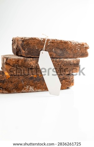 Three stacked rustic weathered bricks with a blank white label hanging on a string, isolated on a white background. Mockup or Copyspace