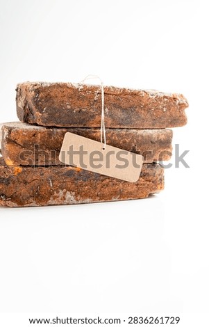 Three stacked rustic, weathered bricks with a blank brown paper label, isolated on a white background. Mockup or Copyspace
