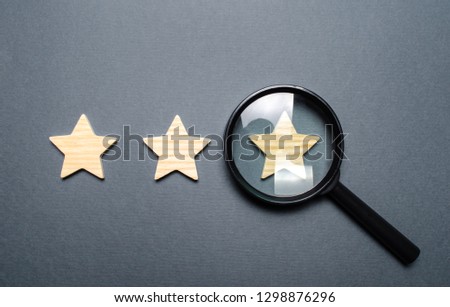 Three stars and a magnifying glass on a gray background. Authentication of the third star, rating fraud. Rating and status of the restaurant or hotel. Prestige.. High quality and reliability