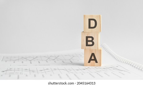 three stone cubes on the background of white financial statements, tables with the word DBA - acronim Doctor of Business Administration. Strong business concept. Gray background.