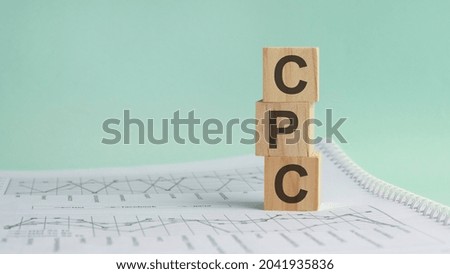 three stone cubes on the background of white financial statements, tables with the word CPC - acronim Cost Per Click . Strong business concept. Gray background.