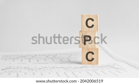 three stone cubes on the background of white financial statements, tables with the word CPC - acronim Cost Per Click . Strong business concept. Gray background.