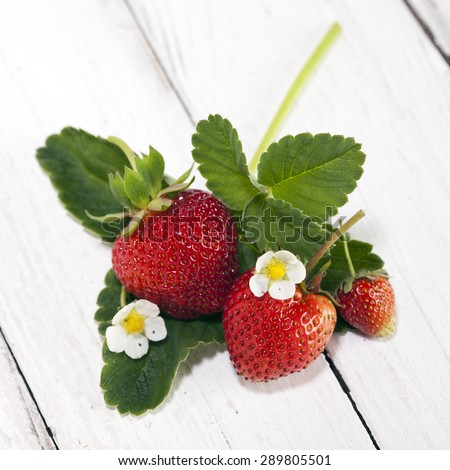 three strawberries with leaves and blossoms arranged on woodensurface