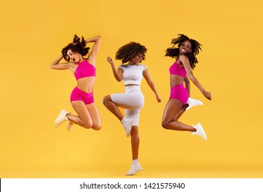 Three Strong And Happy Athletic Women, Jumping Or Dancing On Yellow Background Wearing Color Sportswear. Fitness And Sport Motivation.