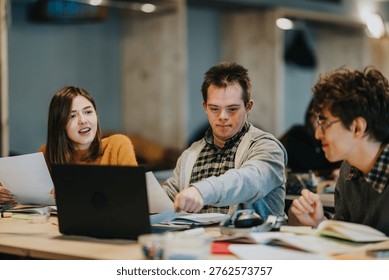 Three students work together at a table with a laptop and study materials. A collaborative study session shows young adults discussing documents and using a computer.