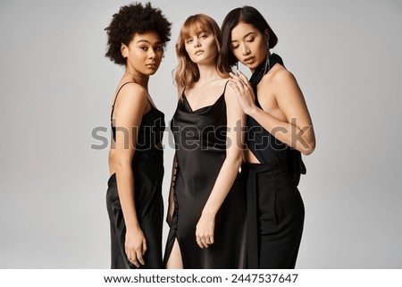 Three stunning women of different ethnicities stand gracefully together against a neutral background.