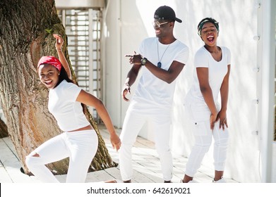 Three Stylish African American Friends, Wear On White Clothes. Street Fashion Of Young Black People. Black Man With Two African Girls Dancing Gangsta Rap Style.