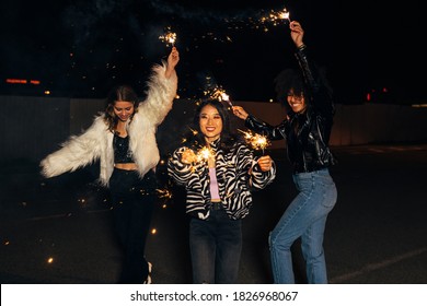 Three Stylish Girls Having Fun While Walking With Sparklers On City Street At Night