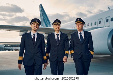 Three Stylish Handsome Pilots Walking Across The Airdrome