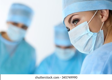 Three surgeons at work operating in surgical theatre saving patient and looking at life monitor. Resuscitation medicine team wearing protective masks saving patient. Surgery and emergency concept - Powered by Shutterstock