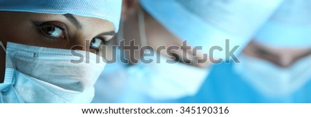 Three surgeons at work operating in surgical theatre. Resuscitation medicine team wearing protective masks saving patient. Surgery and emergency concept. Female surgeon portrait looking in camera