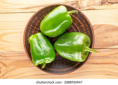 Three sweet green peppers with a clay dish on a wooden table, close-up, top view.