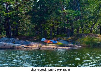 Three Tandem Canoe Upside Down On A Rocky Shore.