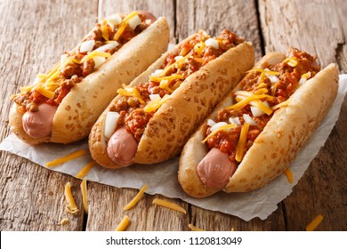 Three tasty chili hot dogs with cheddar cheese, onion and spicy sauce close-up on paper on the table. horizontal - Powered by Shutterstock
