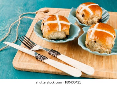 Three tasty Easter cross-buns served on chopping board on blue wooden background
