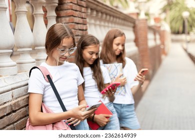 Three teenage girls (14-15 years old) sitting outdoors, absorbed in their phones, exemplify the modern teen (generation Z) lifestyle, education, and the influence of gadgets and social media. - Powered by Shutterstock