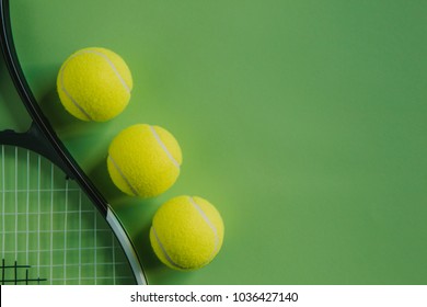Three tennis balls and a racket on green background with copy space on the right.