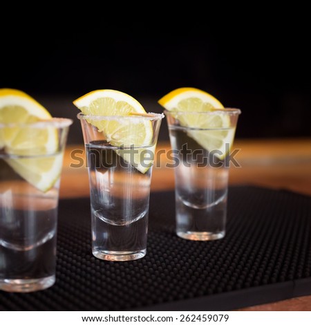 Three tequila shots with lemon on a bar ribber mat. Shallow DOF and toned