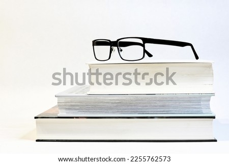  three thick books on a table with glasses as a visual aid and a white background                               