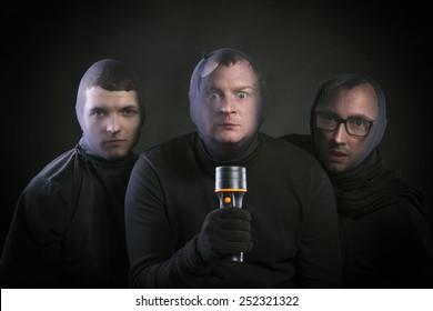 Three thieves in balaclavas on their faces, dressed in black. Studio shot on black background.