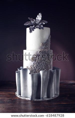 Three tiered stylish large wedding cake decorated with beads and silver flower on top. food design. trends