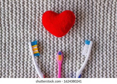 Three Toothbrushes And A Red Heart On A Knitted Gray Background. Two Adults, One Children's Toothbrush And Heart. Love, Relationships, Harmony, Family Concept And Valentine's Day, Family With A Child