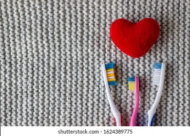 Three Toothbrushes And A Red Heart On A Knitted Gray Background. Two Adults, One Children's Toothbrush And Heart. Love, Family Concept And Valentines Day, Family With A Child. Copy Space