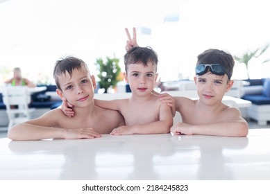 three topless little boys are sitting at the table of a summer bar and laughing and playing horns to each other. Summer vacation
