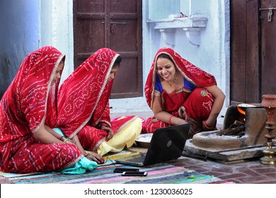 Three traditional Indian young married women working in traditional kitchen on laptop. Using technology in rural households. Women cook food and learn technology. Rural women using Laptop. 