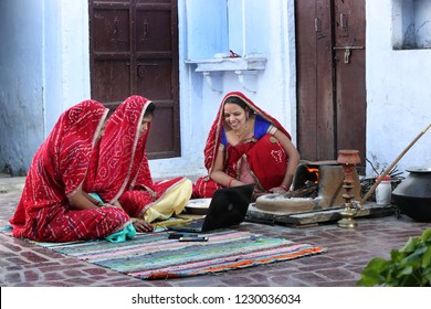 Three Traditional Indian Young Married Women Working In Traditional Kitchen On Laptop. Using Technology In Rural Households. Women Cook Food And Learn Technology. Rural Women Using Laptop. 