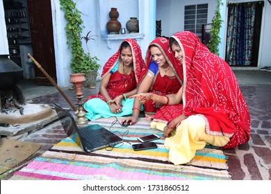 Three traditional Indian young married women working in traditional kitchen on laptop. Using technology in rural households. Women learn technology. Rural women using Laptop.