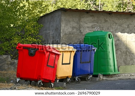 Three trash cans are lined up next to a building. The trash cans are red, yellow, and green