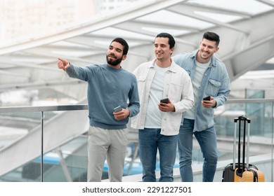 Three Travelers Men Using Smartphones Pointing Finger Aside Standing With Suitcase In Modern Airport Indoor. Passengers Advertising New Travel App. Mobile Services For Tourists - Shutterstock ID 2291227501
