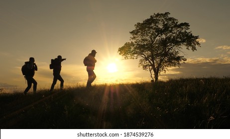 three travelers walk along top of hill past a lone tree in sun. teamwork of tourists with backpacks following route. concept of hiking travel and outdoor adventure, in park, field and mountains. - Powered by Shutterstock