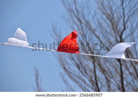 Three triangular flags, two white and one red, are strung on a thin line against a vibrant blue sky.