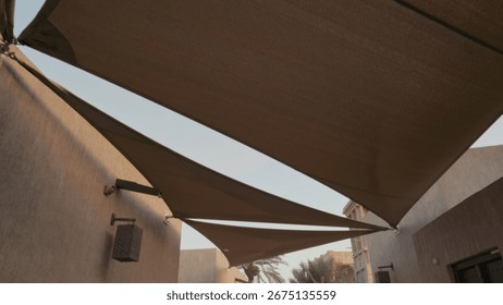 Three triangular shade sails provide coverage in a calm residential courtyard. Serene outdoor setting enhances peaceful atmosphere during daytime.