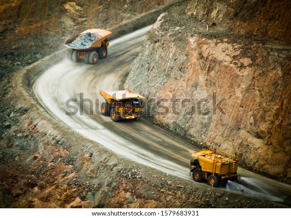 Three trucks in a\
busy modern gold mine in Kalgoorlie, Western Australia. One water\
truck and two large haul trucks transport gold ore from an open\
cast mine. - All logos\
removed.