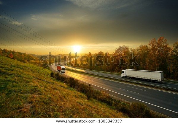 Three trucks driving on\
the asphalt highway in autumn landscape at sunset                  \
            