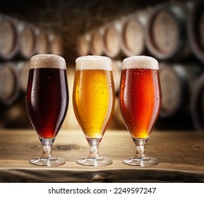 Three type of beer with foam head on wooden table. Blurred brewery cellar at the background. - Powered by Shutterstock