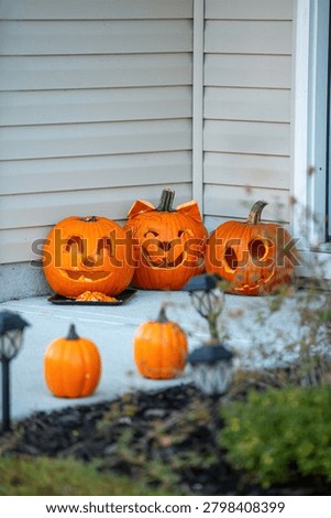 Three unlit jack- o' -lanterns on a porch with orange pumpkins.