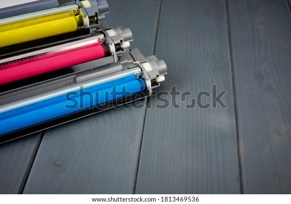 Three used toner cartridges in a\
color laser printer on gray wooden background for\
recycling