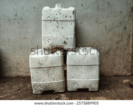 Three used white plastic containers that were already worn out were stacked in the corner of the yard wall.