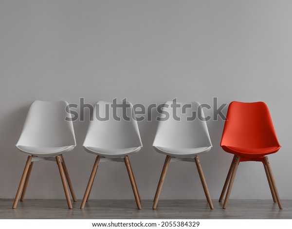 Three vacant white chairs and one red on gray wall\
background in office or room. Simple minimalist interior, nobody,\
free space. Job recruiting, leadership and business due covid-19\
virus, mockup
