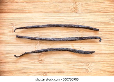 Three vanilla pods aligned on wooden background