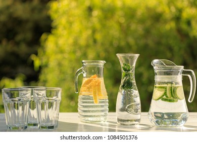 Three variants of fresh homemade lemonade with lemon, cucumber and mint. Lemonade in jugs and carafe on garden. 